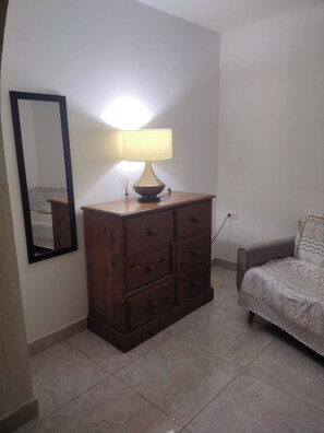 Une pièce comprenant une commode en bois, un lit avec une literie à motifs et un miroir fixé au mur.