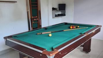 A pool table with balls, two pendant lights, a clock, and a shelf with electronic devices.