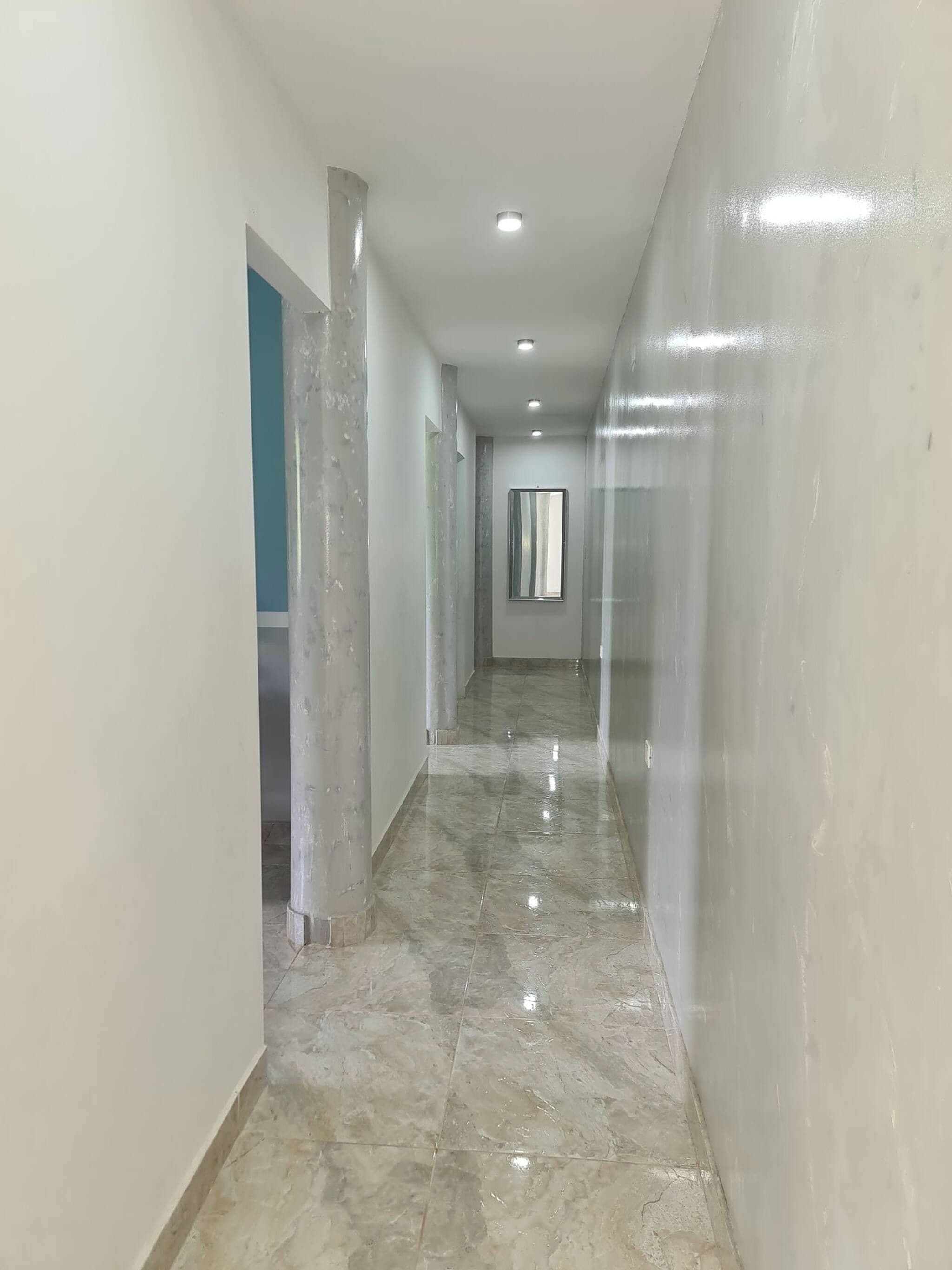 A corridor with a glossy floor, white walls, and a recessed ceiling light.