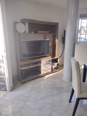 Un salon équipé d’un téléviseur à écran plat, d’un meuble de rangement en bois et d’un fauteuil.
