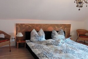 A bedroom with a bed, two nightstands, a lamp, and two wicker chairs. - Imperial on the Eifelsteig (Gerolstein)