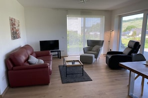 A living room with a red sofa, a grey armchair, a black armchair, a TV, and a table with a lamp. - ||-----------------------Above the Moselle 1--------------------|| (Bernkastel-Kues Andel)