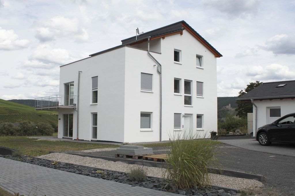 Ein modernes, zweistöckiges Haus mit flachem Dach, großen Fenstern und einem kleinen Balkon.