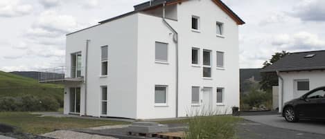 Ein modernes, zweistöckiges Haus mit flachem Dach, großen Fenstern und einem kleinen Balkon.