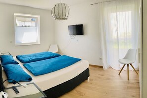 Une chambre à coucher moderne avec un lit, un téléviseur fixé au mur, une fenêtre avec des stores et un fauteuil.
