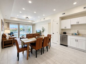 A modern kitchen with white cabinets, a dining area with a wooden table and brown chairs, and a view of the outdoors through large sliding doors. - New Pigeon Forge Condo | Mt. Views (Pigeon Forge)