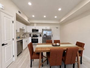 A modern kitchen with white cabinetry, stainless steel appliances, and a dining area with a wooden table and brown chairs. - New Pigeon Forge Condo | Mt. Views (Pigeon Forge)