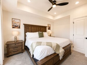 A bedroom with a wooden bed, two bedside lamps, a ceiling fan, and a door. - New Pigeon Forge Condo | Mt. Views (Pigeon Forge)