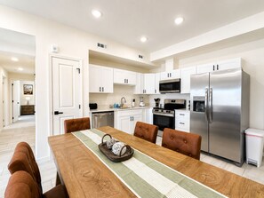 A modern kitchen with white cabinets, stainless steel appliances, and a dining area with a wooden table and leather chairs. - New Pigeon Forge Condo | Mt. Views (Pigeon Forge)