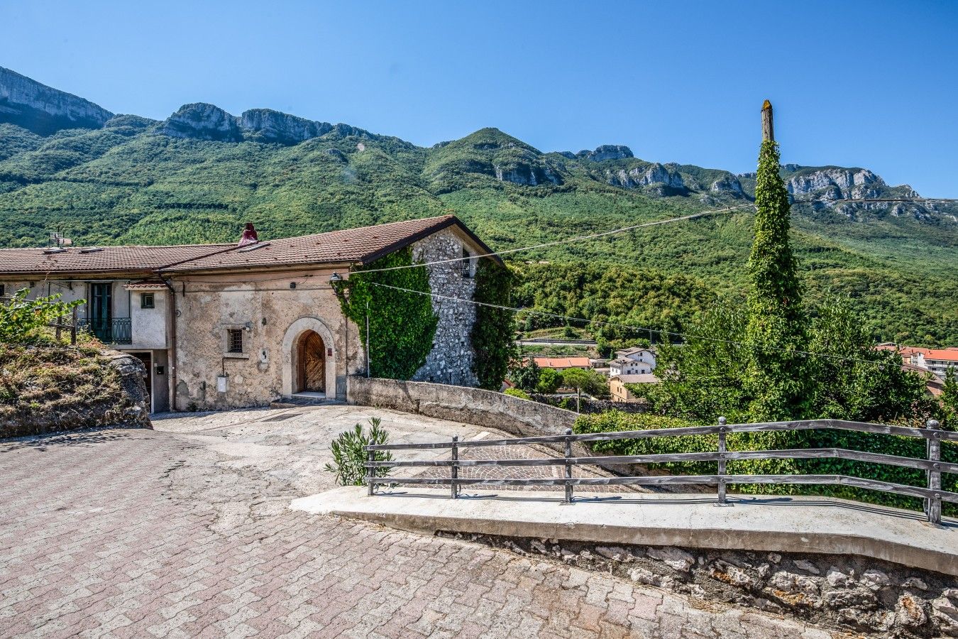 Un edificio in pietra con tetto in tegole, ingresso pavimentato e una parete di pietra.