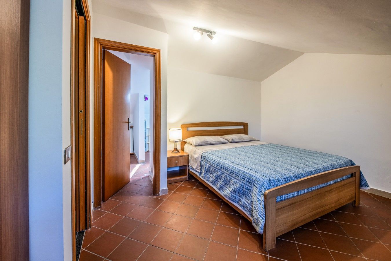 Una camera da letto con un letto in legno, un comodino e una porta che dà su un'altra stanza.
