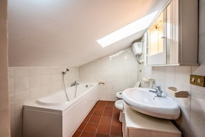 A modern bathroom with a bathtub, toilet, and sink, featuring white fixtures and a sloped ceiling with skylight.