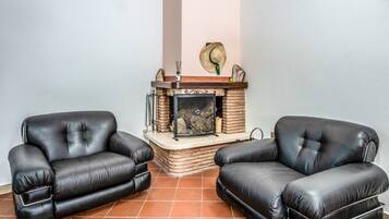 Une pièce avec deux fauteuils en cuir noir, une cheminée avec un manteau en pierre et un sol carrelé.