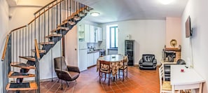 Un interno moderno con una scala a chiocciola, un'area pranzo con un tavolo rotondo e un soggiorno con camino.
