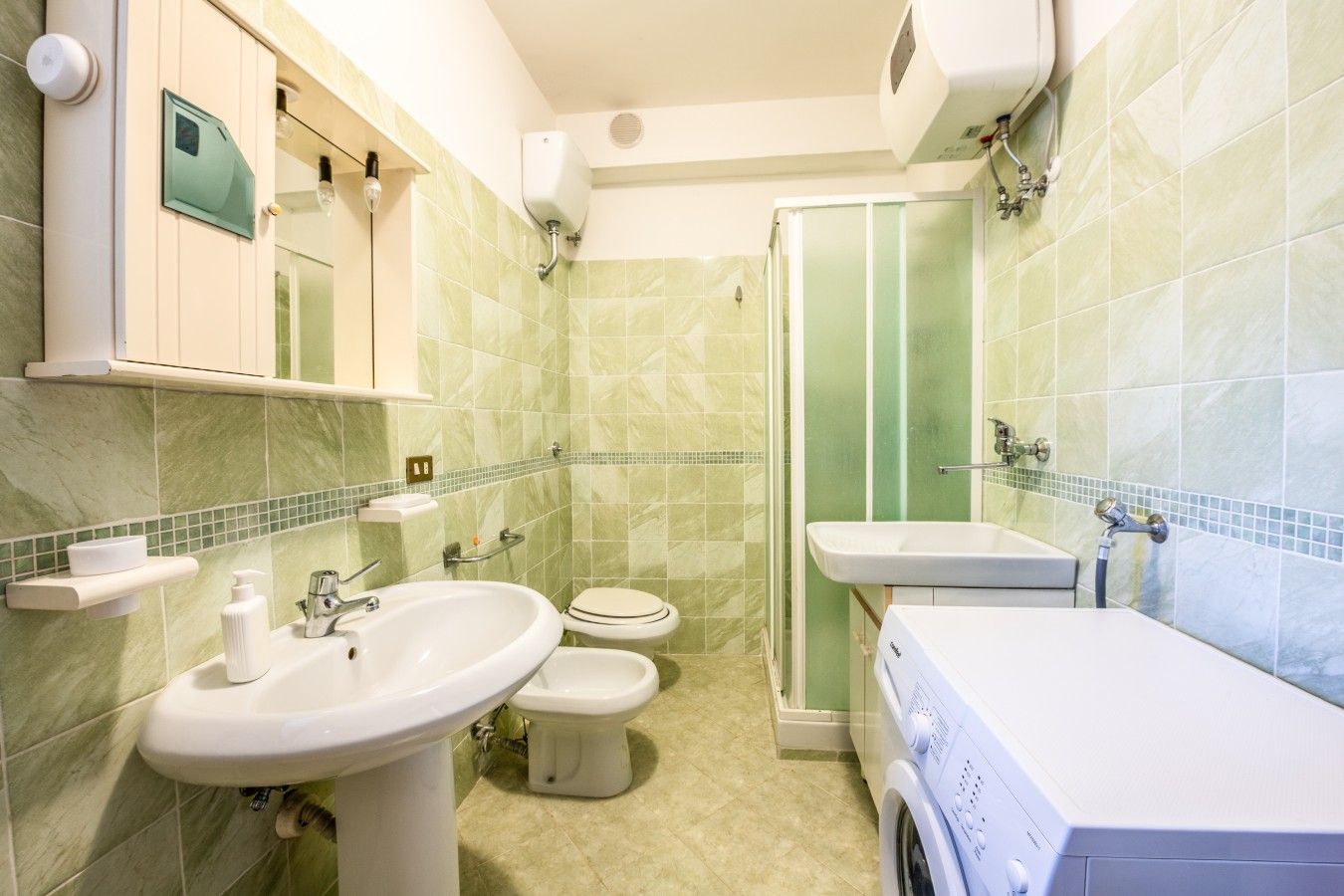 Une salle de bain équipée d’un lave-linge, de deux éviers, de toilettes et d’une cabine de douche.