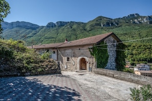 A stone building with a tiled roof, an arched entrance, and a view of a mountainous landscape.