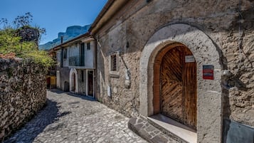 Una stretta strada acciottolata fiancheggiata da edifici storici in pietra, una porta in legno e un cartello che indica un punto di riferimento locale.