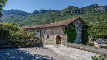 A stone building with a tiled roof, an arched entrance, and a view of a mountainous landscape.
