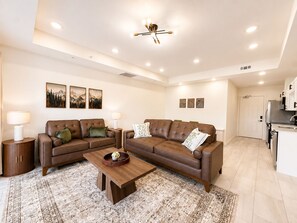 A modern living room with a brown leather sofa, a wooden coffee table, and a patterned rug. - New Pige Forge Condo | Steps to Parkway (Pigeon Forge)
