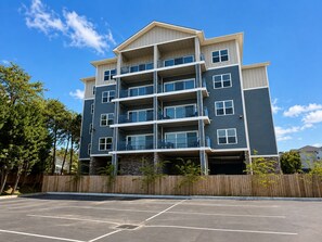 A multi-story residential building with balconies, a parking lot in front, and a wooden fence. - New Pige Forge Condo | Steps to Parkway (Pigeon Forge)