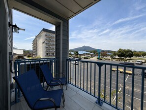 A balcony with two chairs, a view of a parking lot, and a building in the background. - New Pige Forge Condo | Steps to Parkway (Pigeon Forge)