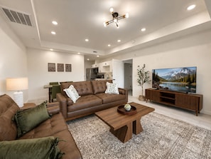 A modern living room with a brown leather sofa, a wooden coffee table, and a flat-screen TV on a wooden stand. - New Pige Forge Condo | Steps to Parkway (Pigeon Forge)