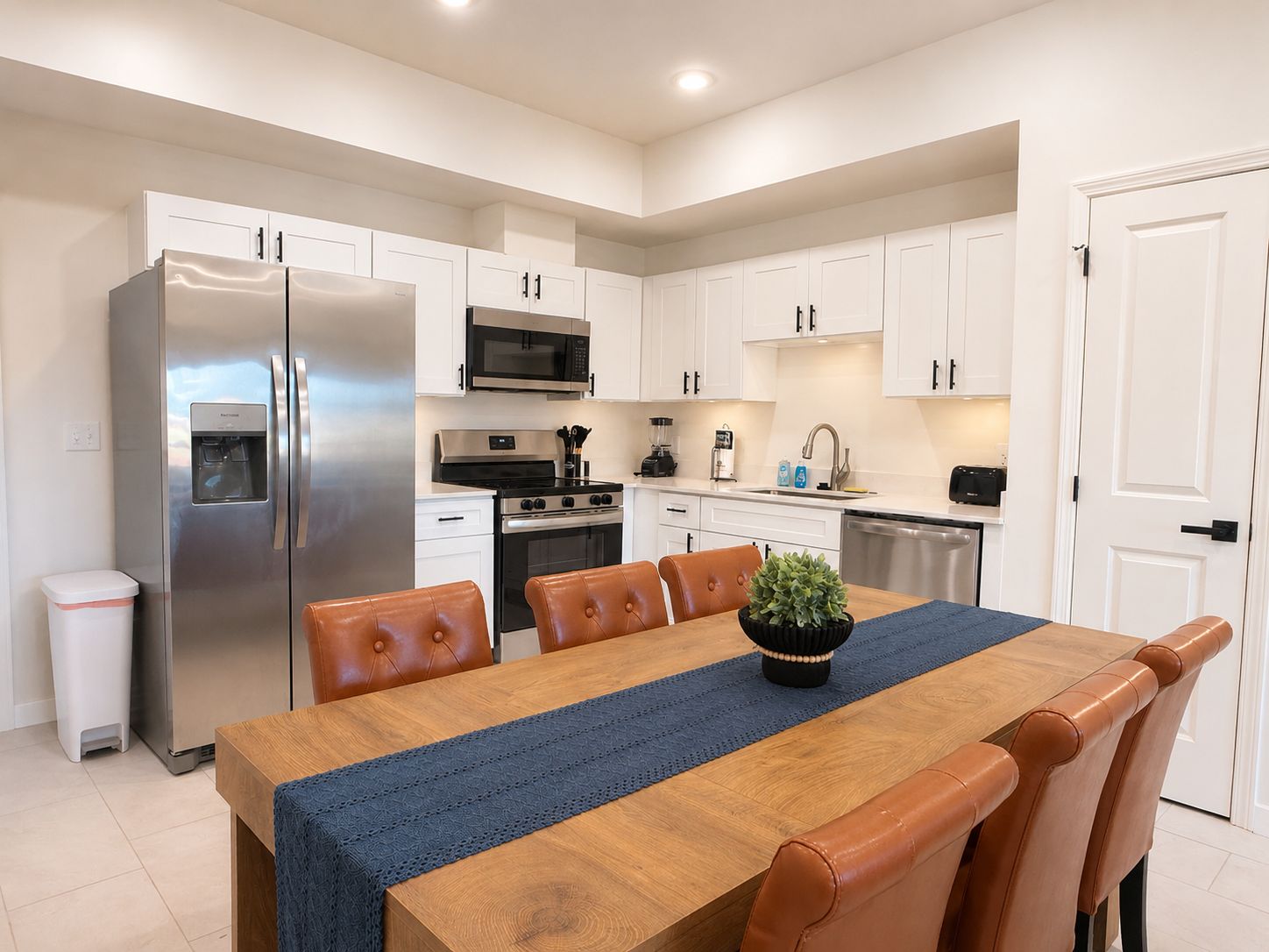 A modern kitchen with white cabinets, stainless steel appliances, and a dining area with a wooden table and leather chairs.
