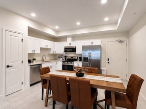 A modern kitchen with white cabinets, stainless steel appliances, and a dining area with a wooden table and brown chairs. - New Pigeon Forge Condo | Island View (Pigeon Forge)