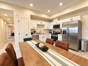 A modern kitchen with white cabinets, stainless steel appliances, and a dining area with a wooden table and brown chairs. - New Pigeon Forge Condo | Mt View (Pigeon Forge)