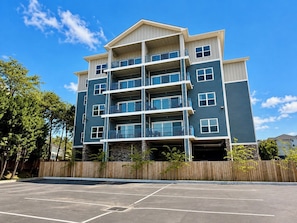 A multi-story residential building with balconies, a parking lot, and a wooden fence. - New Pigeon Forge Condo | Mt View (Pigeon Forge)