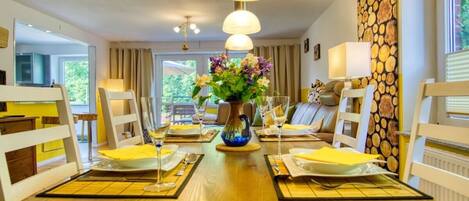 A dining area with a wooden table set for four, surrounded by white chairs, with a vase of flowers in the center.