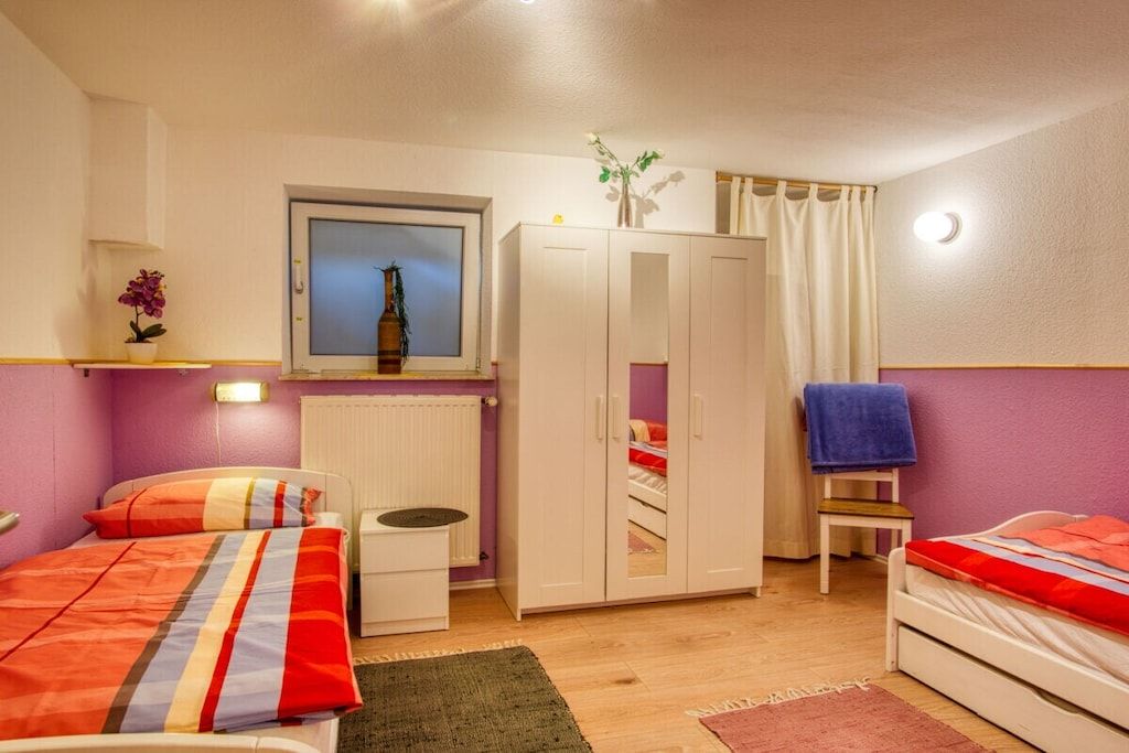Une chambre avec deux lits, une armoire, une petite table, un radiateur et une fenêtre donnant sur un beau paysage.