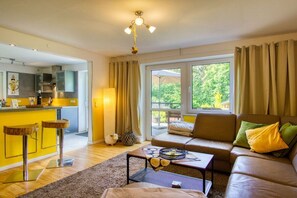 A living room with a sofa, a coffee table, and a kitchen area in the background. - Holiday apartment with 2 bedrooms (Amelinghausen)
