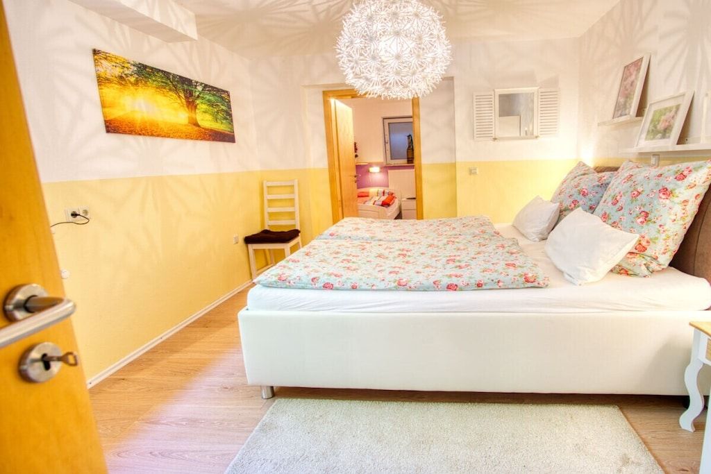 Une chambre à coucher avec un lit, un luminaire suspendu, une porte avec une poignée et un tableau accroché au mur.
