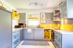 A modern kitchen with grey cabinets, a yellow accent wall, and a window providing natural light. - Holiday apartment with 2 bedrooms (Amelinghausen)