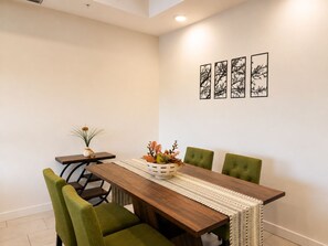 A dining area with a wooden table, green upholstered chairs, and a woven table runner. - New Pige Forge Condo | Steps to Parkway (Pigeon Forge)