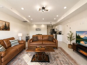 A modern living room with a brown leather sofa, a coffee table, and a fireplace. - New Pige Forge Condo | Steps to Parkway (Pigeon Forge)