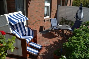 Eine Terrasse mit Korbstühlen, einem Tisch und einem Sonnenschirm.