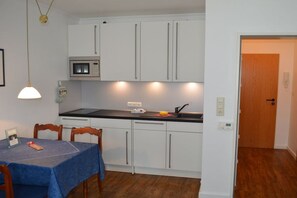 A compact kitchen with white cabinets, a microwave, and a dining area with a table and chairs. - Holiday apartment with 1 bedroom (Wangerooge)