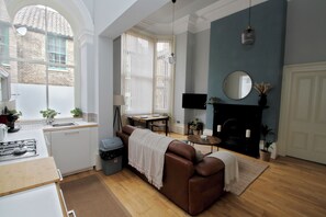 A modern kitchen with a gas stove, a dining area with a table and chairs, a brown leather sofa, and a fireplace. - Historic Hull Old Town Apartment (Kingston upon Hull)