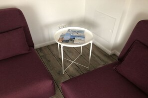 Ein Zimmer mit zwei violetten Sesseln, einem kleinen weißen Tisch mit Zeitschriften und einem Holzboden.