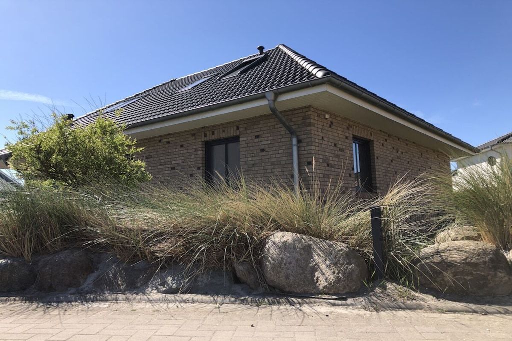 Une maison en briques avec un toit en tuiles, entourée de gros rochers et d’herbes hautes.