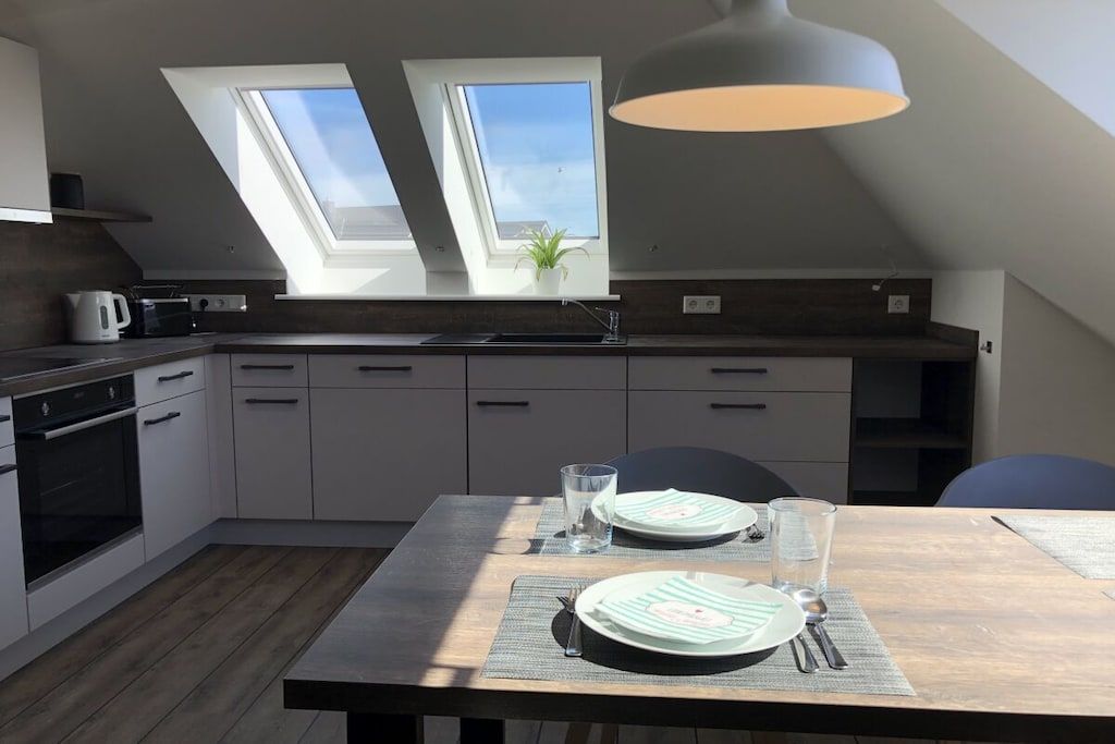 Une cuisine moderne dotée de fenêtres de toit, d’une table à manger préparée pour deux personnes et d’un luminaire suspendu.