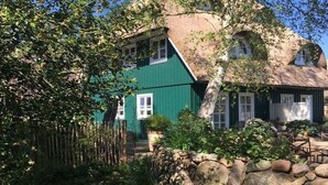 A traditional house with a steeply pitched roof, surrounded by a stone wall and lush greenery.