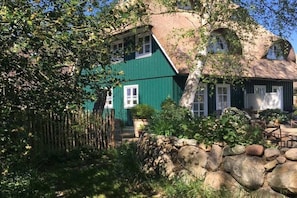 A traditional house with a steeply pitched roof, surrounded by a stone wall and lush greenery.