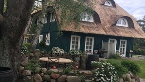 A rustic house with a thatched roof, stone walls, and a small outdoor seating area with a table and chairs.