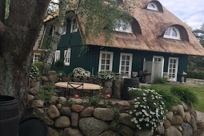A rustic house with a thatched roof, stone walls, and a small outdoor seating area with a table and chairs.