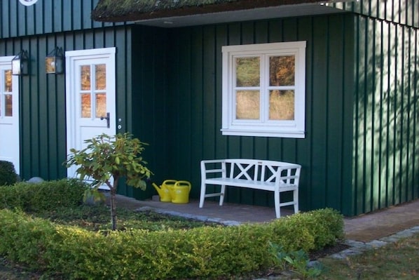 A green building with a white bench and a small tree.