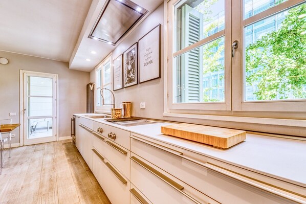 A modern kitchen with a large window, a built-in oven, and a countertop with a cutting board.