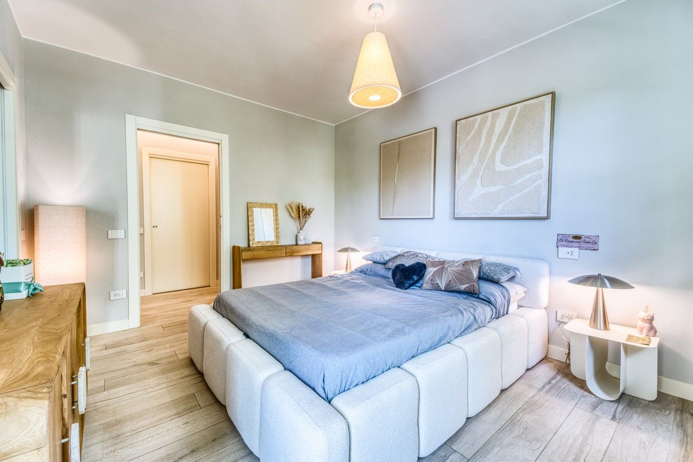 Ein Schlafzimmer mit einem Bett, Nachttischen, einer Lampe und Kunstwerken an den Wänden.